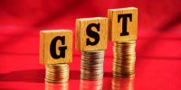 Wooden letters GST and money coin stack on red table background, financial concept